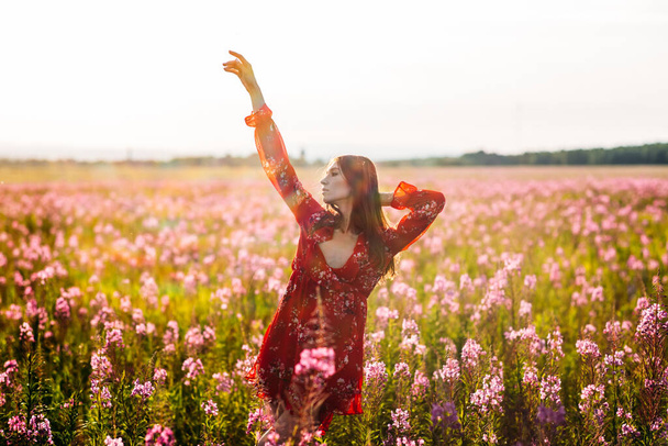 Hermosa, alta, joven, pelo largo, vestido rojo en un campo con flores rojas
. - Foto, Imagen