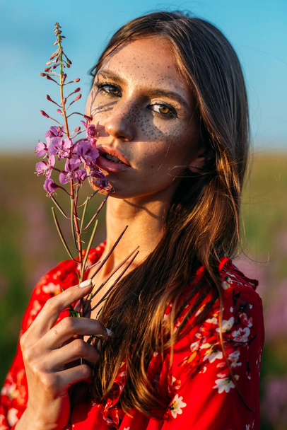 Beautiful, tall, young girl, long hair, red dress in a field with red flowers. - Фото, изображение