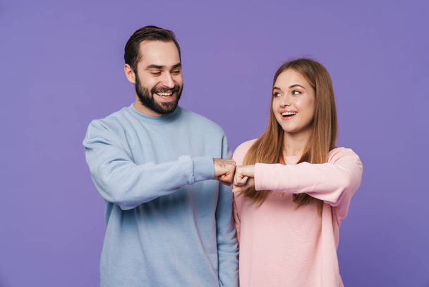 Picture of happy positive optimistic loving couple posing isolated over purple background giving fist bamp. - Foto, Imagem