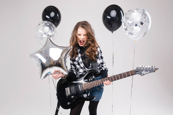 Cute baby girl rock star playing electric guitar and singing song surrounded by balloons - Foto, imagen