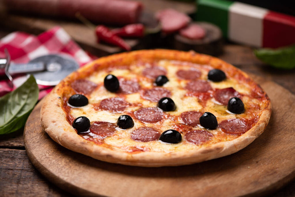 Delizioso salame piccante al forno fresco o pizza al salame piccante con formaggio fuso e olive su una tavola di legno da vicino
 - Foto, immagini