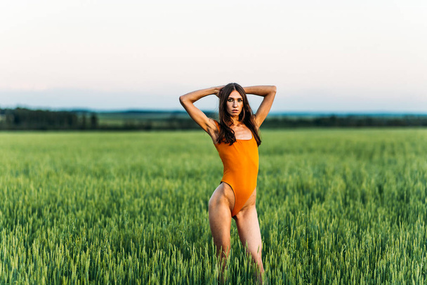 Beautiful girl in a bright bodysuit, Brunette with long hair, alone in a green field, evening light, greenery, sun. - Photo, image