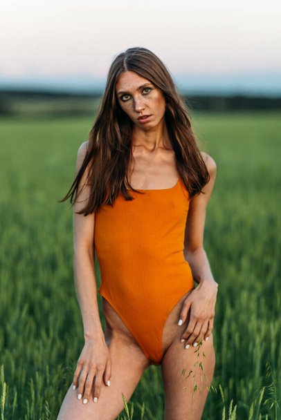Beautiful girl in a bright bodysuit, Brunette with long hair, alone in a green field, evening light, greenery, sun. - Photo, image