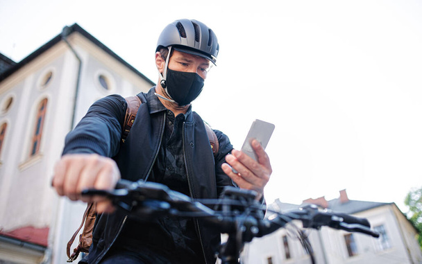 Delivery man courier with face mask and bicycle using smartphone in town. - Foto, imagen