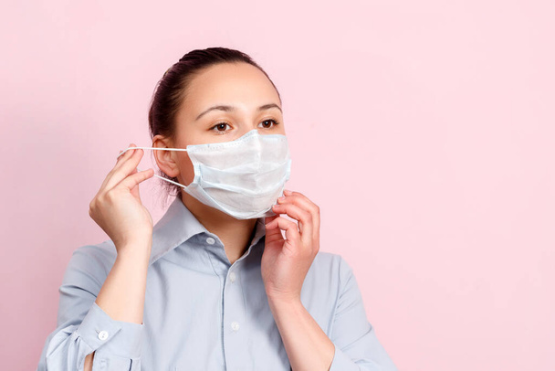 Studio portrait of young woman wearing a face mask, looking at camera, close up, isolated on pink background. Flu epidemic, dust allergy, protection against virus. City air pollution concept - Fotó, kép