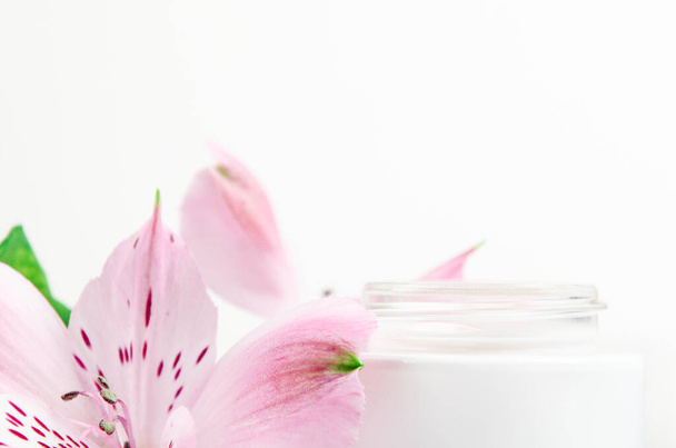 Crema facial en tarro blanco sobre fondo blanco con flores rosas. Concepto cosmética natural, belleza orgánica, arreglo floral. Copiar espacio
 - Foto, imagen
