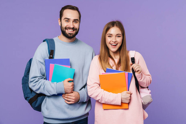 Photo of a positive happy loving couple friends students isolated over purple wall background holding books. - Фото, зображення