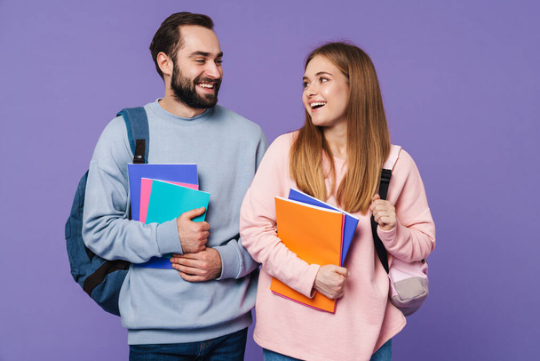 Photo of a cheery loving couple friends students isolated over purple wall background holding books. - Fotografie, Obrázek