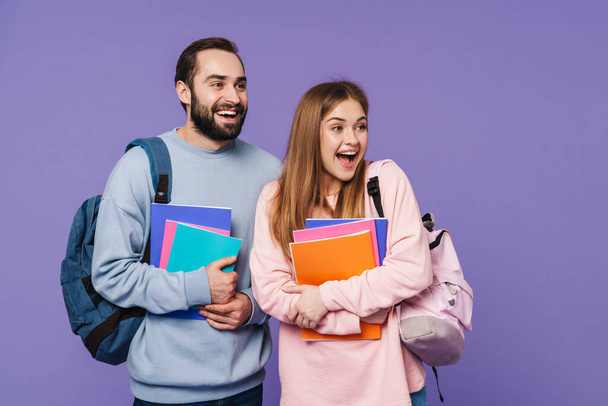 Photo of a positive happy loving couple friends students isolated over purple wall background holding books. - Valokuva, kuva