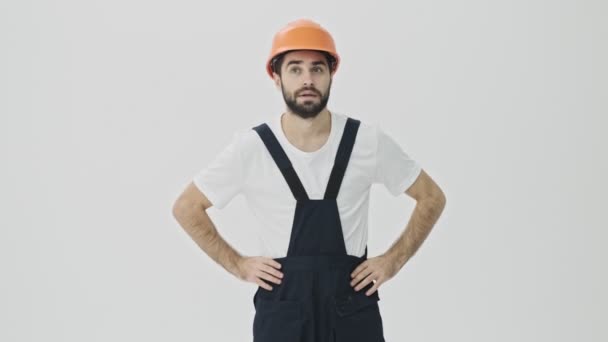 Handsome concentrated young bearded man builder isolated over white wall background in helmet. - Video, Çekim