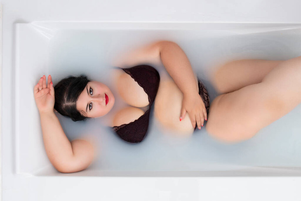 mujer en lencería sensual de color rojo oscuro en una bañera lechosa
. - Foto, Imagen