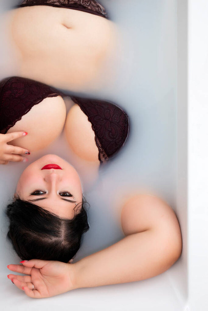 Frau in sinnlichen dunkelroten Dessous auf einer milchigen Badewanne. - Foto, Bild