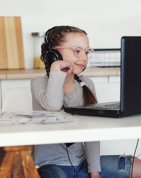 Κορίτσι με φορητό υπολογιστή και ακουστικά στην εκπαίδευση του σχολείου στο σπίτι. Μάθηση σε εξέλιξη. - Φωτογραφία, εικόνα