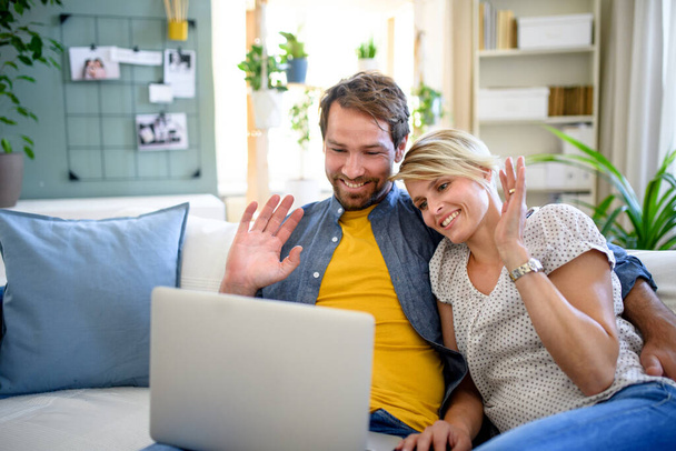 Szczęśliwa para mając wideo rozmowy na laptopie w domu, machając. - Zdjęcie, obraz