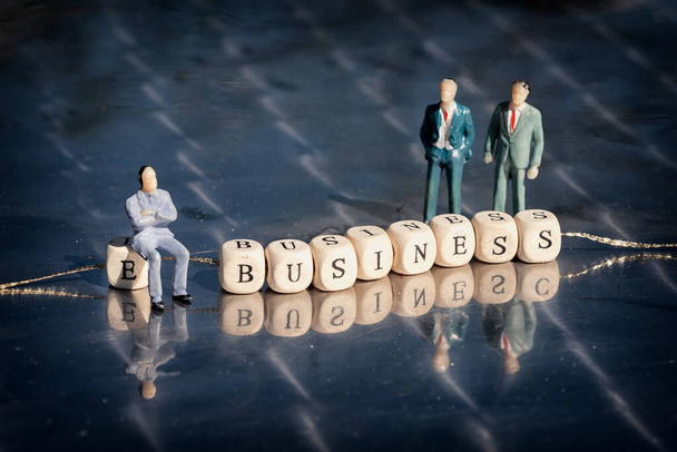 Miniaturowy model biznesmenów i drewnianych kostek z napisem biznesowym na nitce na refleksyjnym stole. Koncepcja biznesowa online. - Zdjęcie, obraz