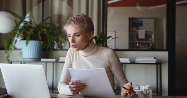 Focused businesswoman using laptop doing paperwork sitting at office desk - 映像、動画