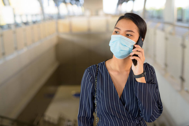 Портрет молодой азиатской предпринимательницы в маске для защиты от вспышки коронного вируса на вокзале Skytrain - Фото, изображение