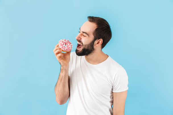 Photo of young happy positive man isolated over blue wall background with donut. - Foto, immagini
