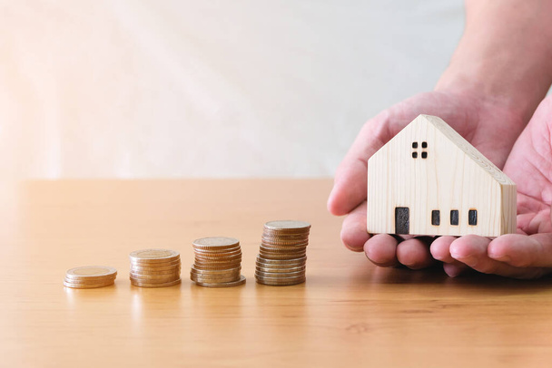 Men hand hold, giving wood house beside increasing money, coin stack on wood table. Saving plan to buy property, house. Personal financial concept for own a house. with copy space for text - Photo, Image