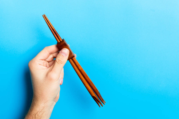 Crop image of male hand holding hopsticks on background. Concept alimentaire japonais avec espace de copie
. - Photo, image