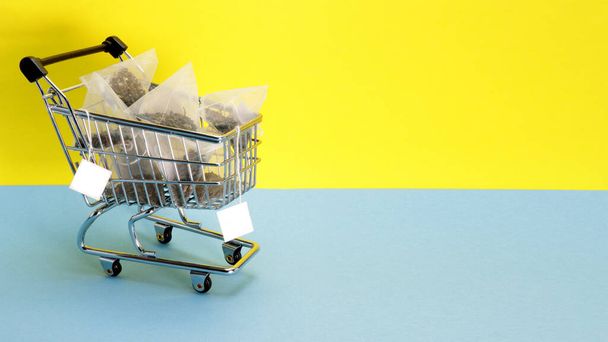 Σακουλάκια τσαγιού σε ένα καρότσι από το μαγαζί. Φωτεινό κίτρινο-μπλε φόντο. Αγορές - Φωτογραφία, εικόνα