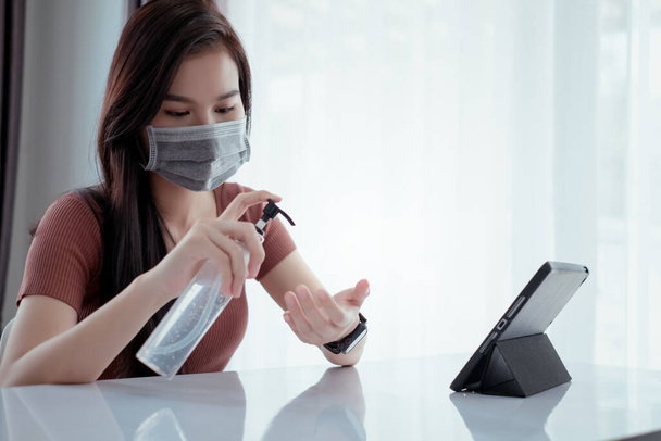 Asian man wearing mask pump hand gel alcohol cleaning sanitizer working from home with laptop computer prevent the spread of coronavirus quarantine workplace with protective stay home. - Фото, изображение