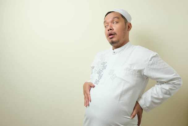 Asiatische muslimische Männer fühlen sich sehr satt, nachdem sie beim Fastenbrechen zu viel gegessen haben. Der Mann hält seinen großen Magen voller Nahrung - Foto, Bild
