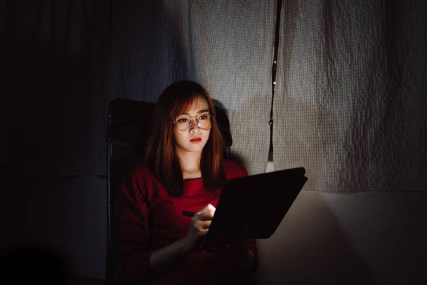 Asian woman working late at night with tablet digital gadget at home office work hard stressed serious emotion, Freelancer stay home business quarantine crisis coronavirus stay home dark room - Fotoğraf, Görsel