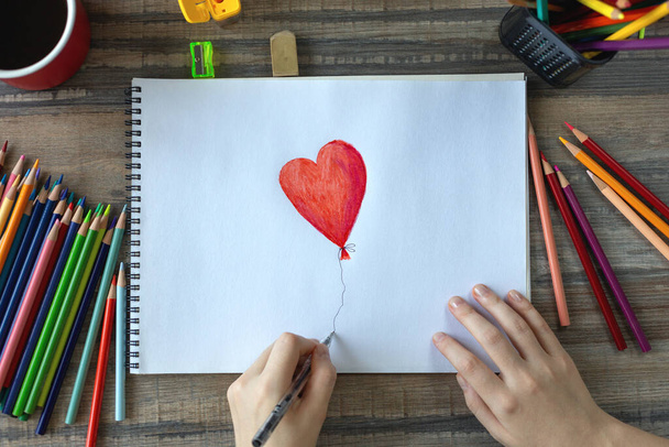 Vlakke handenlegger die een hart tekent met gekleurde potloden op wit papier. Art studio werkplek concept - Foto, afbeelding