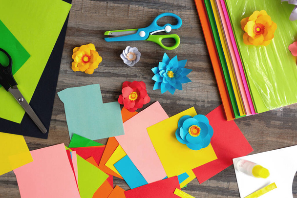 Плоская укладка цветных цветных бумажных цветов и ножниц на деревянном столе. Концепция рабочего места арт-студии
 - Фото, изображение