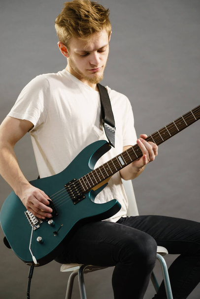 Young bearded man with electric guitar. Adult person is holding instrument and playing. Hobby, music concept, on grey - Fotó, kép