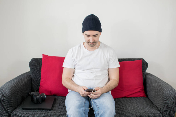 mladý muž sedět na gauči detailní obsah tvůrce práce z domova blogger freelancer notebook kamera držet smartphone typ - Fotografie, Obrázek
