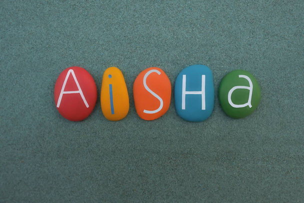 Aisha, αραβικά γυναικείο όνομα που αποτελείται από πολύχρωμα πέτρινα γράμματα πάνω από την πράσινη άμμο - Φωτογραφία, εικόνα
