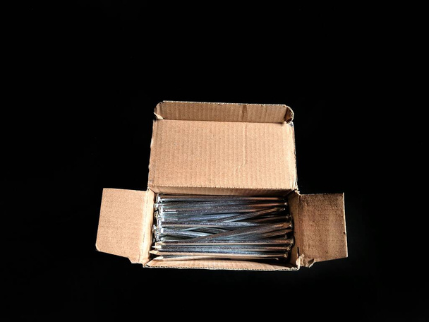 Steel nails inside a cardboard box on black background. construction concept - Photo, Image