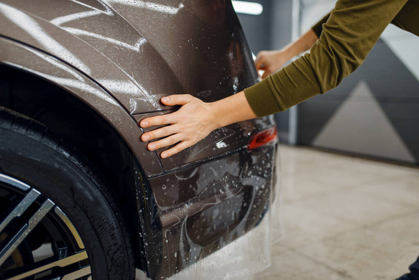A munkás autóvédő fóliát használ a hátsó lökhárítón. Beépítése bevonat, amely megvédi a festék az autó a karcolásoktól. Új jármű a garázsban, hangolási eljárás - Fotó, kép