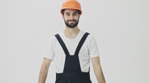 Happy cheery young bearded man builder isolated over white wall background in helmet - Imágenes, Vídeo