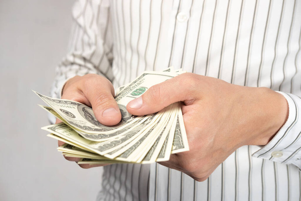 Ein Mann (Geschäftsmann) in hellem Hemd hält Geld in seinen Händen. Zählt Bargeld (Hundert-Dollar-Scheine)). - Foto, Bild