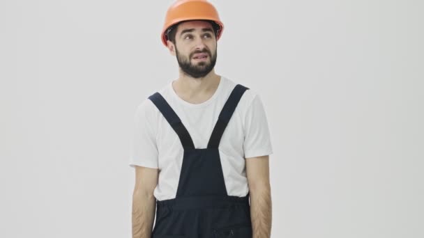 Confused young bearded man builder isolated over white wall background in helmet - Séquence, vidéo