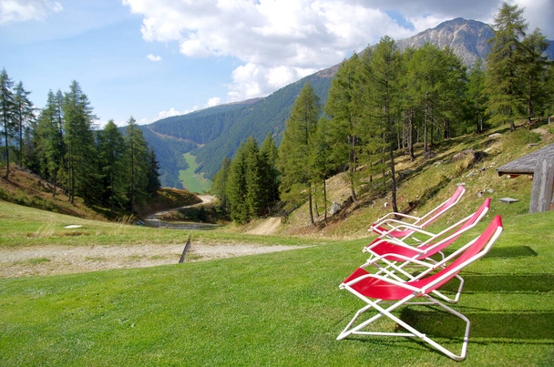червоні крісла для відпочинку туристів і захоплення високих гір зеленими луками і пишними лісами і гострими скелями під блакитним небом
 - Фото, зображення
