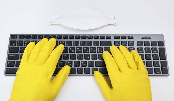 A man in bright yellow rubber gloves is typing on the keyboard. Disinfection in public places, the fight against the virus, coronavirus. - Valokuva, kuva