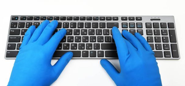 A man in blue rubber gloves is typing on the keyboard. Disinfection in public places, the fight against the virus, coronavirus. - Fotoğraf, Görsel