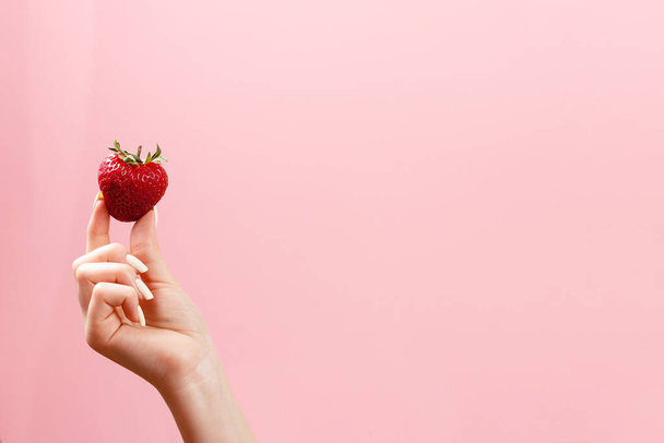 Woman holds strawberry in hand on front of pink background. - Foto, immagini
