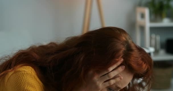 Großaufnahme eines kaukasischen rothaarigen traurigen verzweifelten Mädchens mit langen lockigen roten Haaren, das zu Hause auf der Couch sitzt und sich große Sorgen macht. Herzzerreißend hoffnungslose junge Frau, die in Schwierigkeiten denkt. Angst. Traurigkeit - Filmmaterial, Video