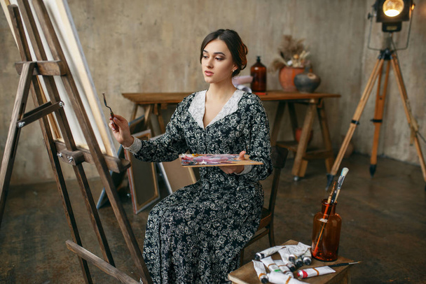 Malířka se štětcem a paletou pózuje v ateliéru umění. Umělec na jejím pracovišti, kreativní mistr na stojanu v dílně - Fotografie, Obrázek