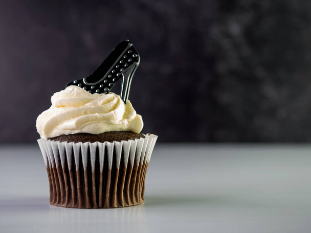 白い霜降りのチョコレートカップケーキは高く渦巻くと黒と銀のポルカドット高いヒールは白いカウンターと黒の大理石の背景と上に座っています。焼き菓子. - 写真・画像