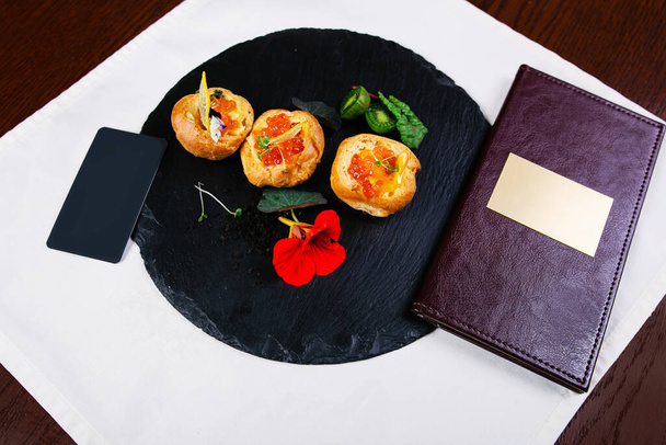 Smoked salmon canape sandwiches with salmon eggs or caviar on a black slate board with fresh parsley leaves, slices of lemon and capers. Overhead view - Zdjęcie, obraz