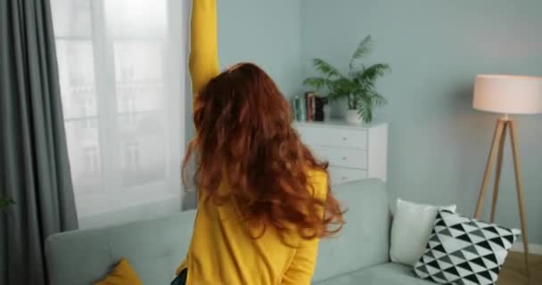 Joyful Caucasian young red-haired woman in yellow sweater dancing and having fun in living room. Happy cheerful female homey dancer at home. Self-isolation leisure time. - Video, Çekim