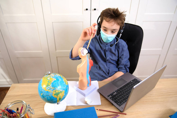 Enseignement à distance en ligne. écolier en masque médical étudiant à la maison, travaillant sur ordinateur portable et faisant des devoirs scolaires. quarantaine de coronavirus
 - Photo, image