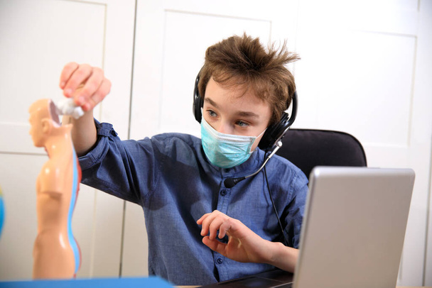 Etäopetus verkossa. koulupoika lääketieteellisessä naamiossa opiskelee kotona, työskentelee kannettavan tietokoneen muistikirjassa ja tekee koulun kotitehtäviä. sepelvaltimoviruksen karanteeni
 - Valokuva, kuva