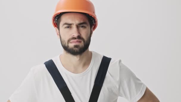 Displeased negative young bearded man builder isolated over white wall background in helmet says no - Кадры, видео